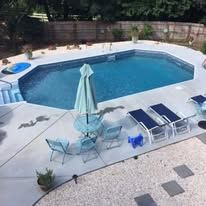 Pool with blue water, surrounded by concrete. Lounge chairs and umbrella are nearby.