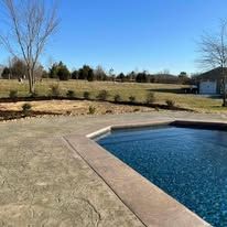 Pool with blue water and surrounding concrete patio on a sunny day.