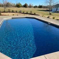 A rectangular swimming pool filled with blue water on a sunny day.