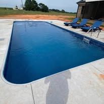 Rectangular outdoor swimming pool with blue water; concrete deck with lounge chairs.