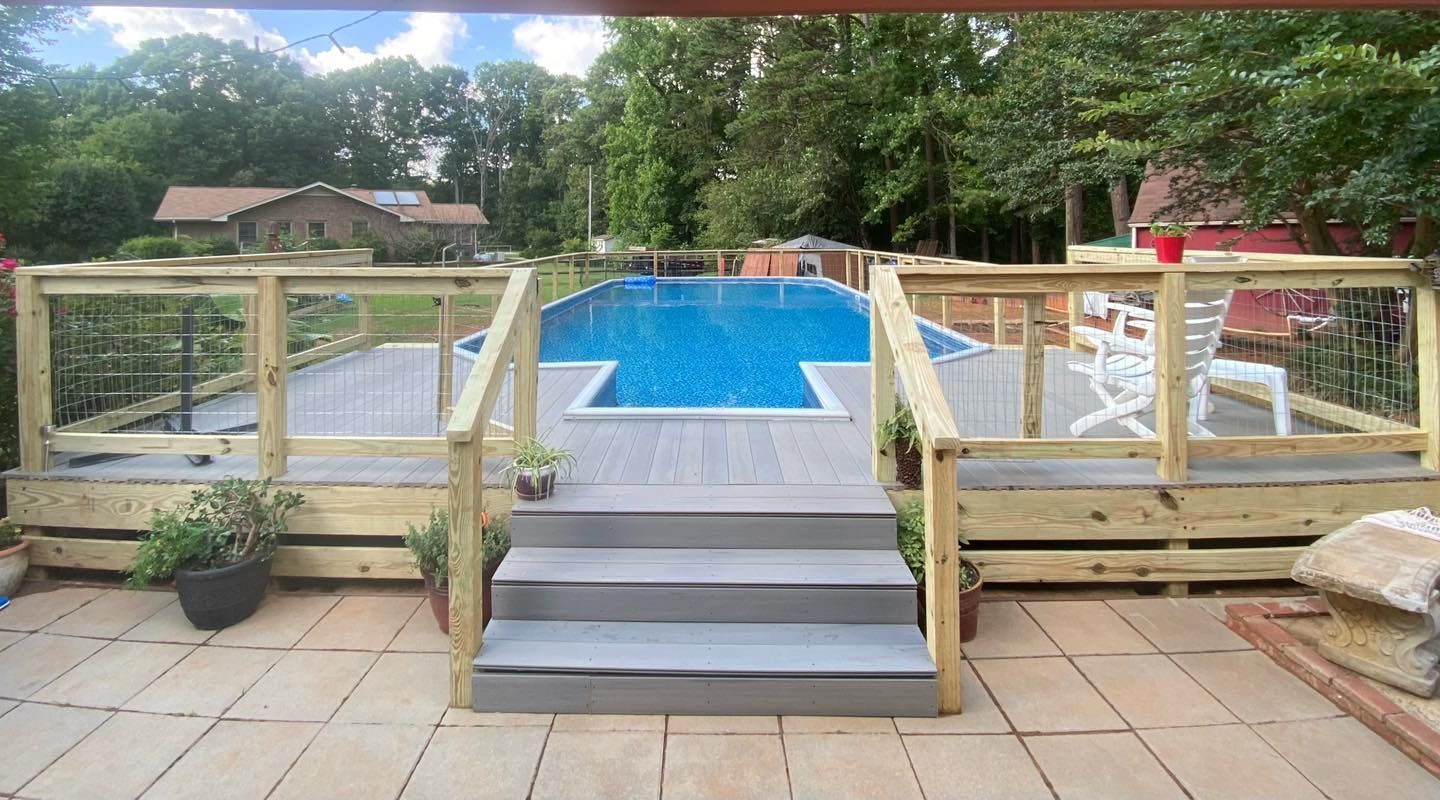 Above-ground pool with deck, stairs, and railing. Lawn and trees in background.