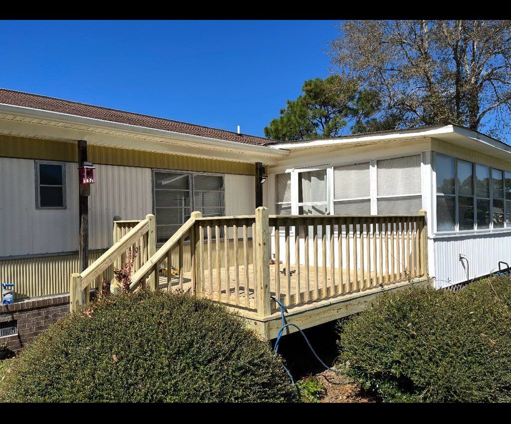 Exterior view of a house with a wooden deck and a sunroom, with bushes in the foreground and a blue sky above.