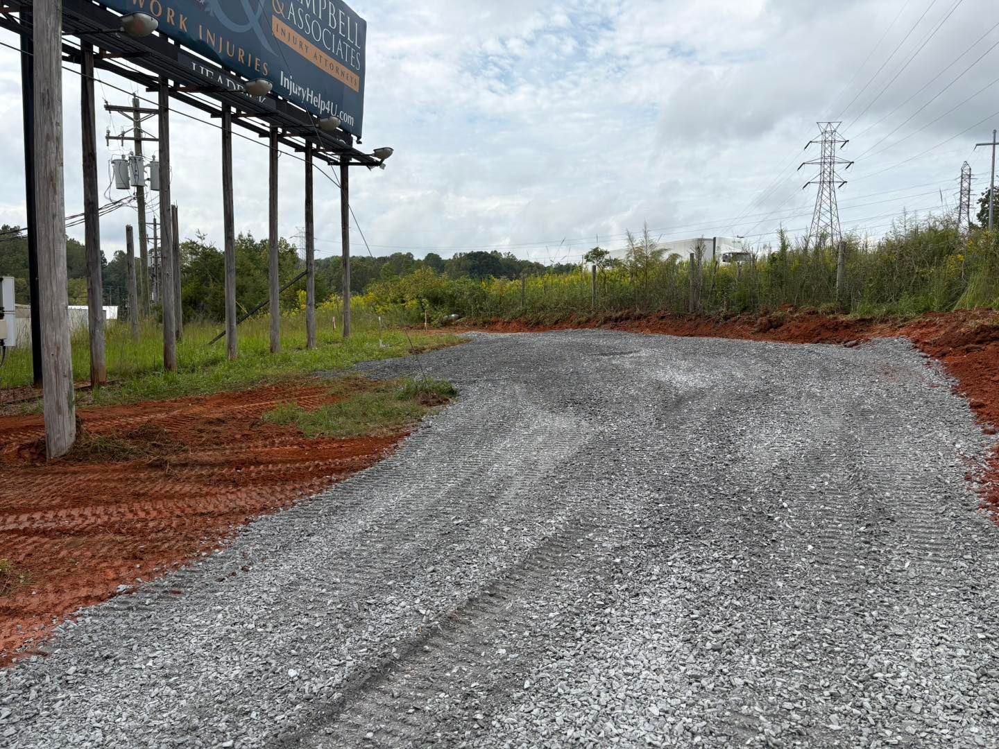 Gravel driveway leading to a grassy area under a cloudy sky. A billboard is on the left.