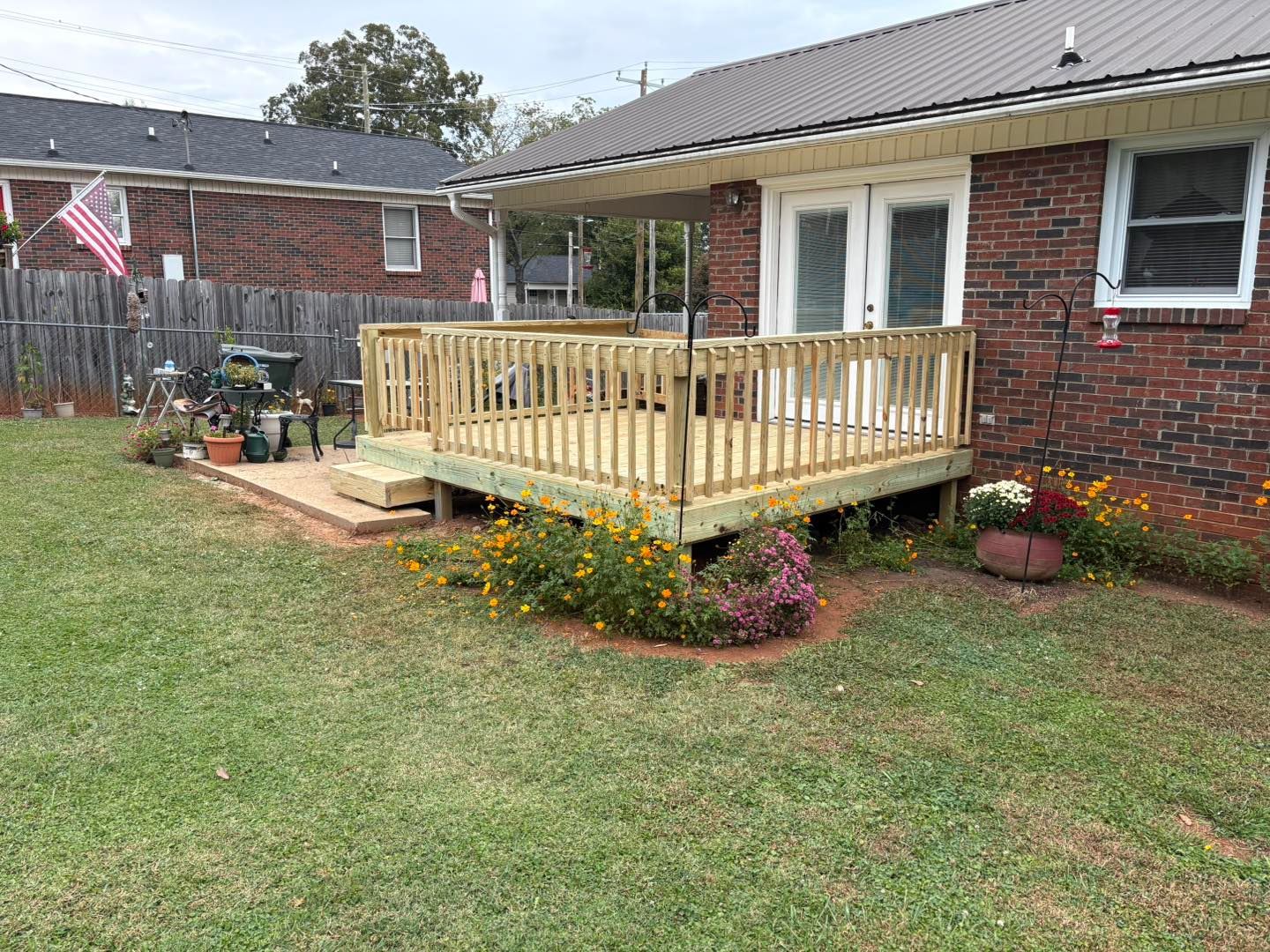 Wooden deck with steps, attached to a brick house. Flowers and green lawn in yard.
