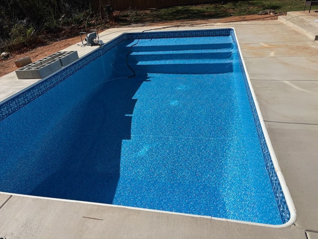 Empty rectangular swimming pool with blue tiled interior and steps, surrounded by concrete.