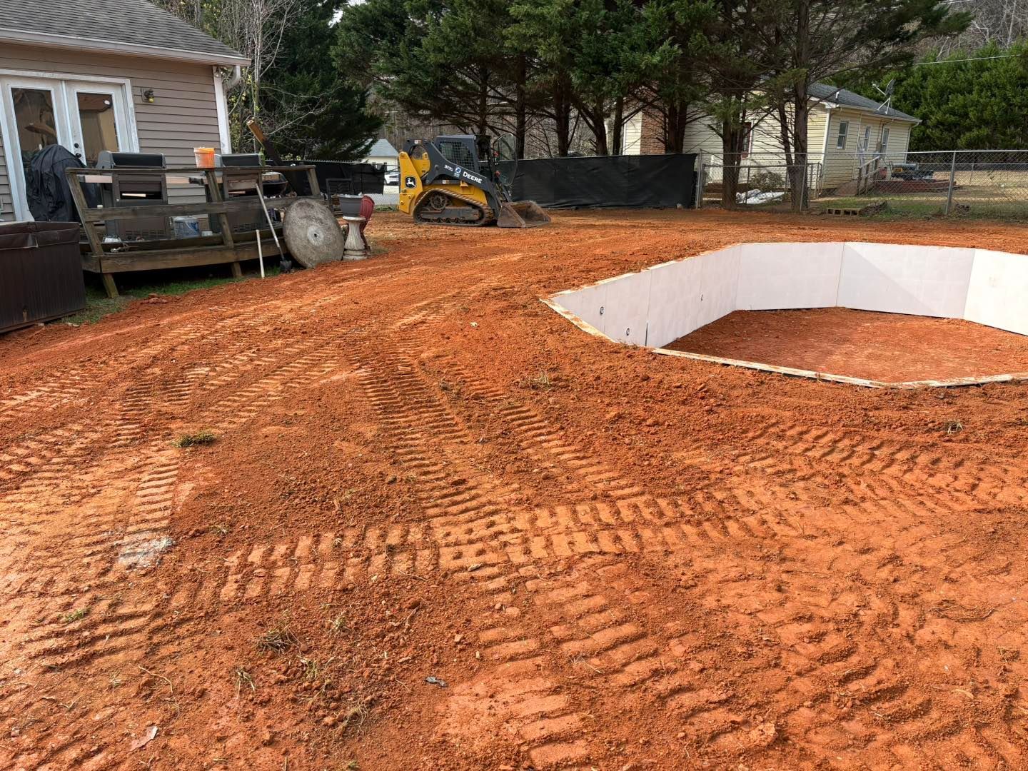 Red dirt yard with an unfinished pool excavation and small tractor.