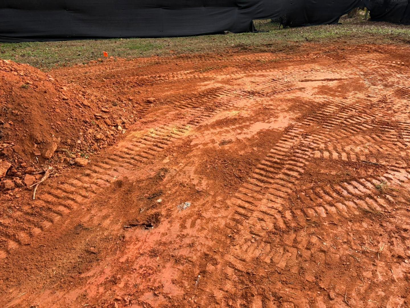 Red dirt ground with tire tracks and a black barrier in the background.