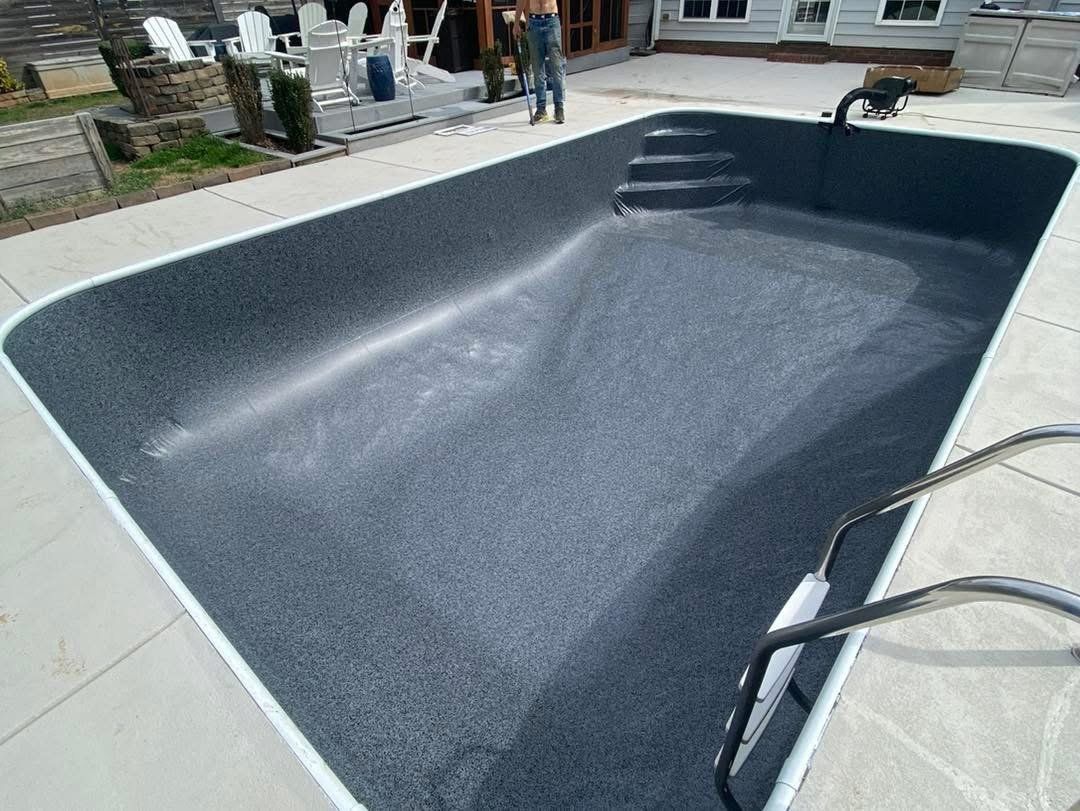 Empty rectangular swimming pool with dark gray interior, concrete border, and metal ladder.