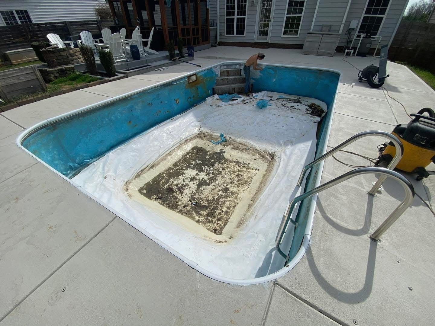 Pool being cleaned with worker, blue sides, white steps, concrete patio.