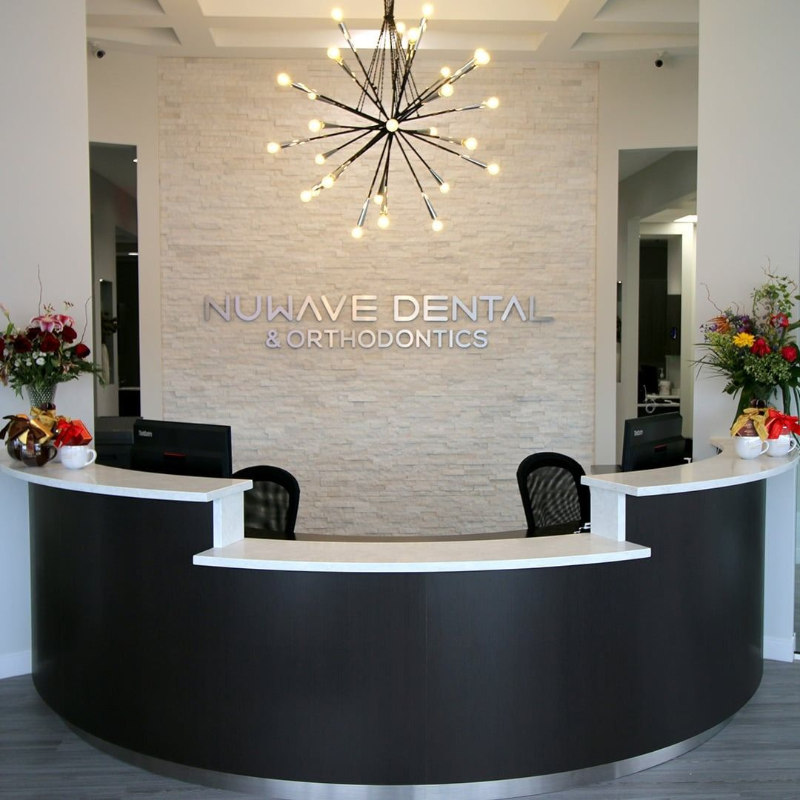 Modern dental office reception desk with black-and-white décor and chandelier, NuWave Dental Orthodontics sign