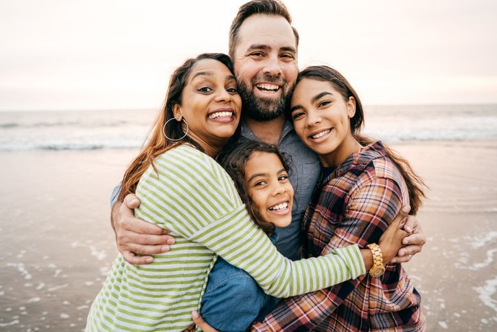 Four friends hugging and smiling on a beach at sunset
