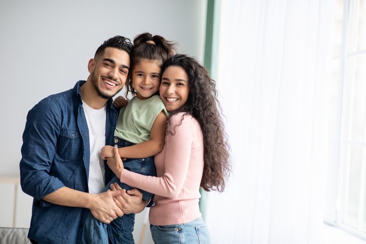 Smiling family hugging indoors by a bright window