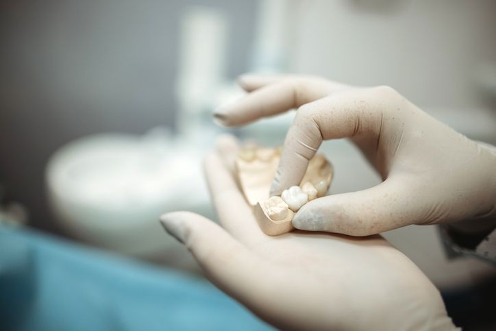 Gloved hands examining a row of artificial teeth in a dental clinic