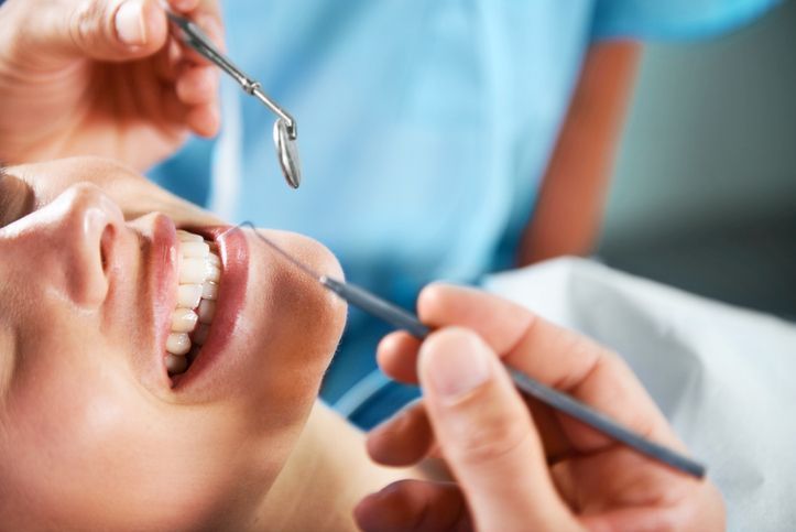 Dentist examining a smiling patient’s teeth with a mirror and dental tool