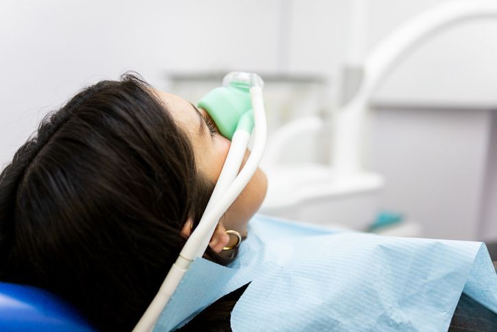Person reclines in a dental chair wearing a green oxygen mask during treatment