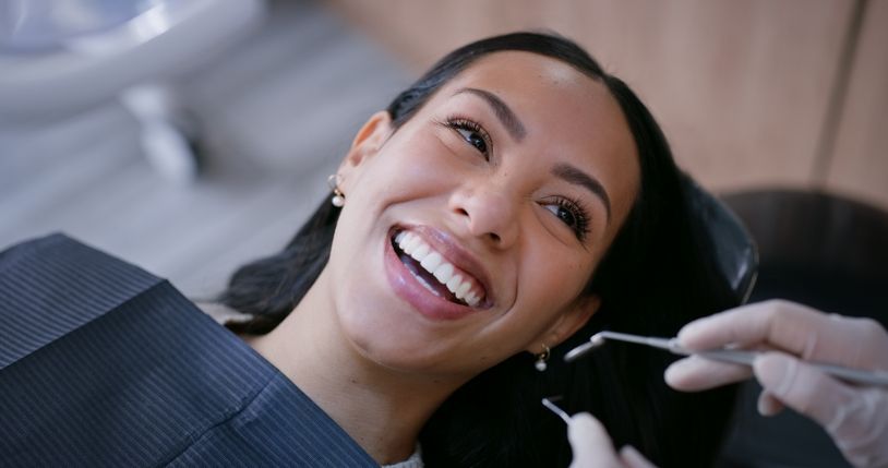 Woman smiling in a dental chair while a dentist uses tools near her mouth