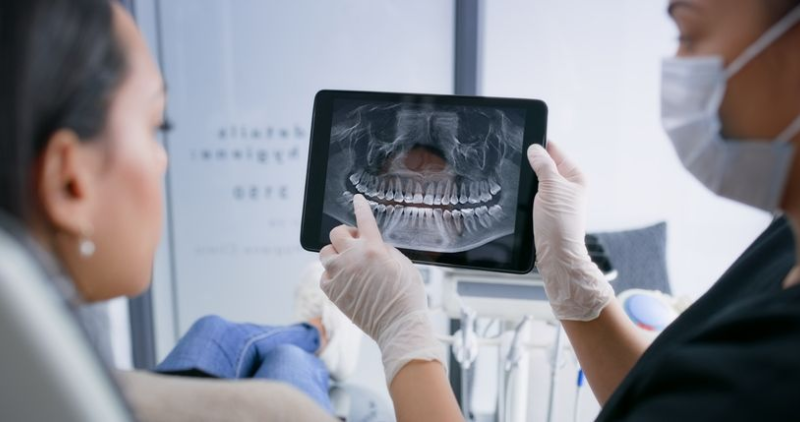 Dentist showing a patient a panoramic dental X-ray on a tablet in a clinic