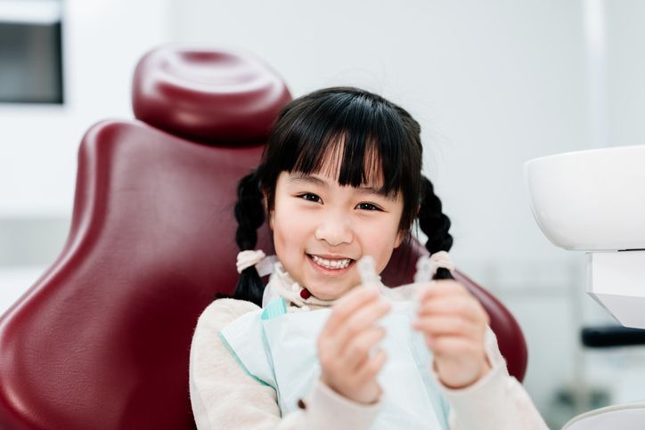 Smiling child in a red dental chair giving a thumbs-up in a bright clinic