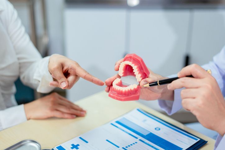 Hands pointing at a dental model with teeth at a clinic desk, alongside a chart.
