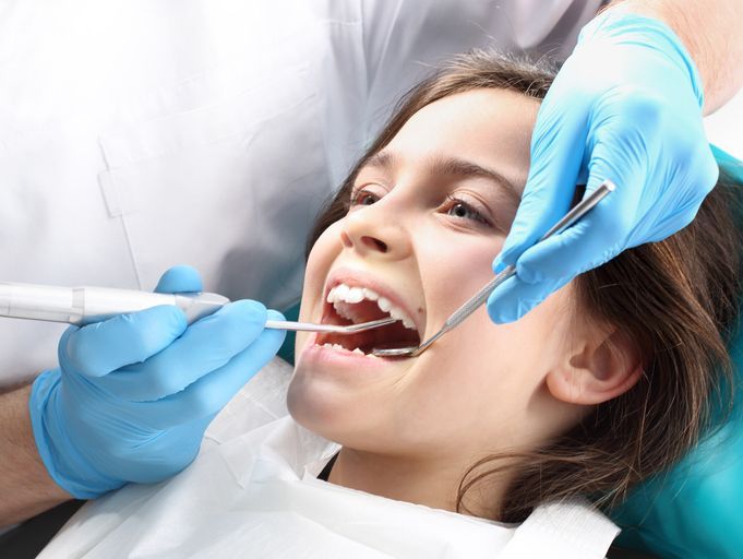 Dentist examining a smiling patient’s mouth with dental tools and blue gloves
