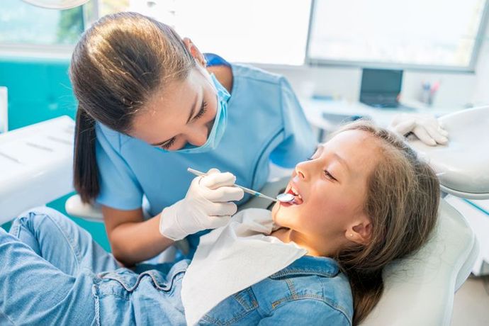 Dentist examining a smiling child in a bright clinic, wearing blue gloves and holding dental tools.