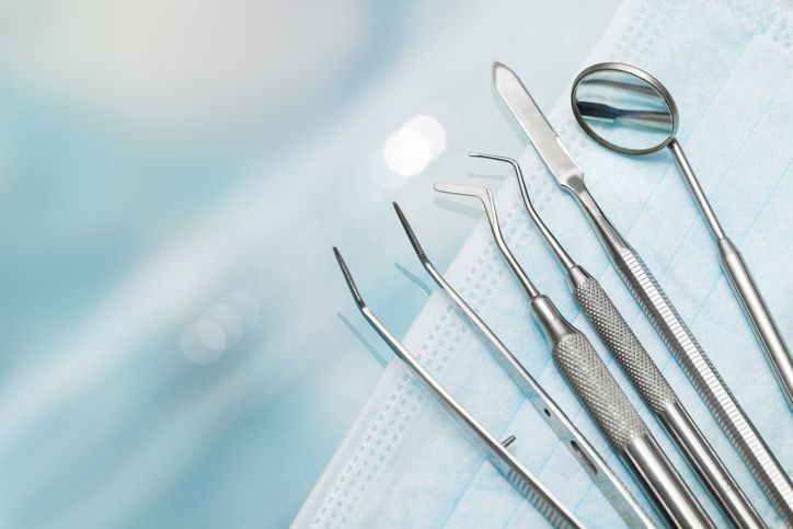 Dental tools on a light blue background, including a mirror, tweezers, and probes.