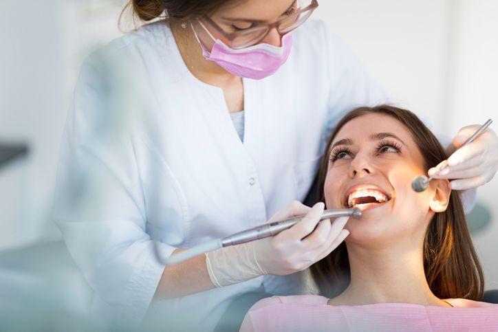 Dentist examining a smiling patient in a dental chair with tools and mask, in a bright clinic