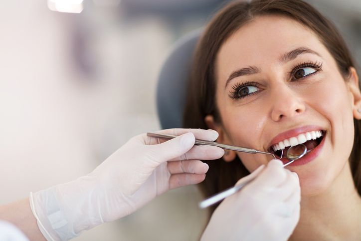 Dentist examining a smiling patient’s teeth with dental tools
