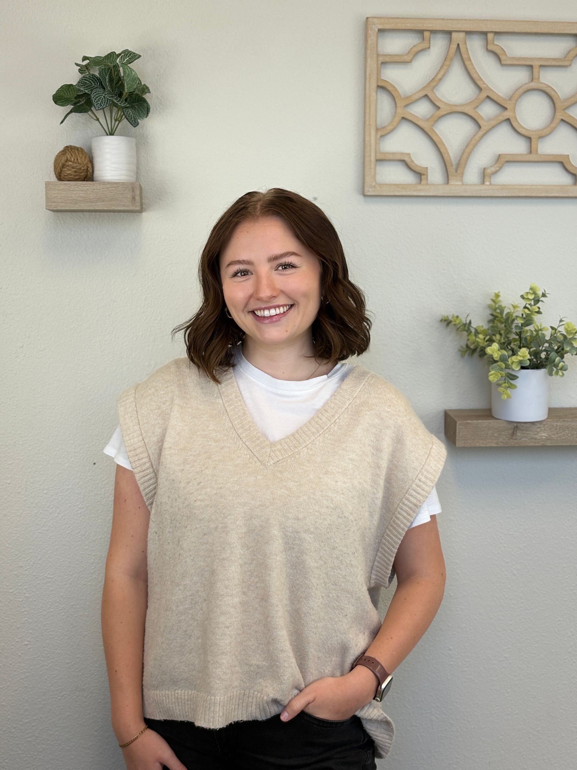 Woman with short brown hair smiles, wearing a tan sweater vest and white shirt.