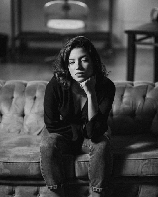 Woman sitting on a couch, resting chin on hand, looking down in thought, black and white.