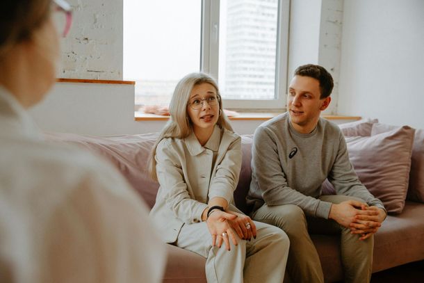 Couple in therapy session, discussing with therapist, neutral tones, indoor setting.