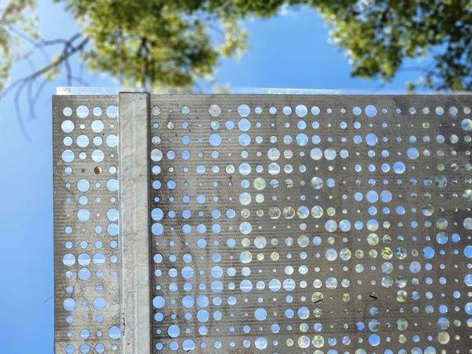 A metal fence with holes in it and a tree in the background.