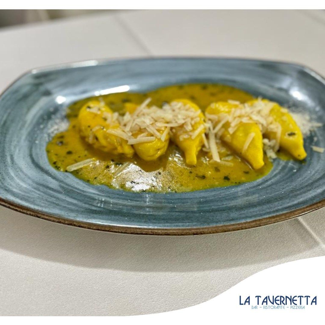 Pasta gialla con sugo e formaggio su un piatto blu.