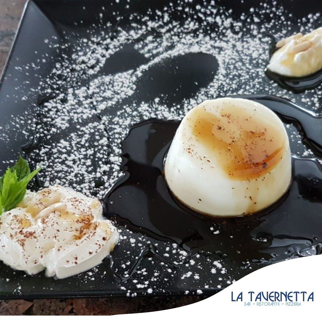 Dessert di panna cotta servito su un piatto nero, condito con salsa, zucchero a velo e panna montata.
