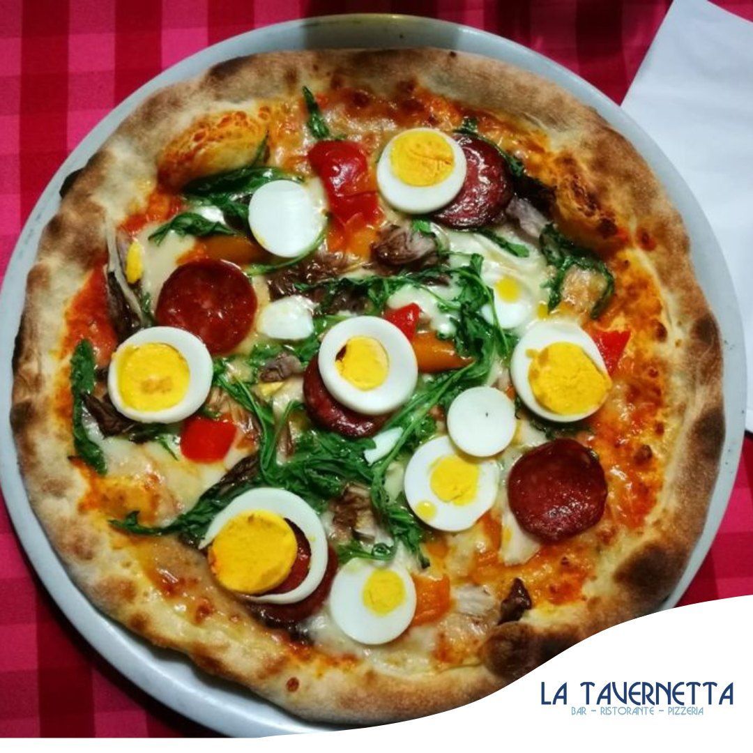 Pizza con uova sode, peperoni e verdure su un piatto bianco.