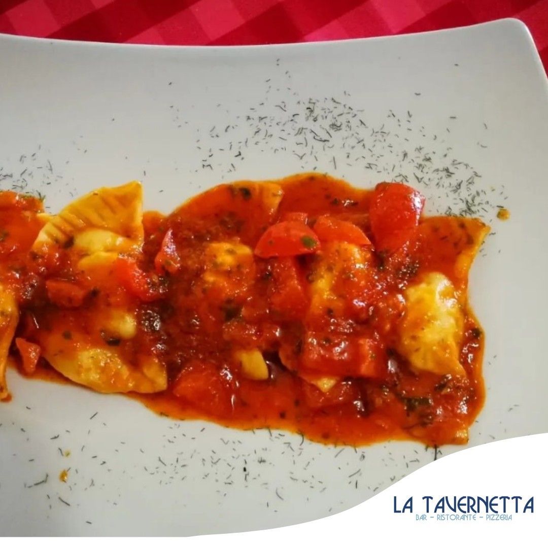 Ravioli con salsa di pomodoro rosso, guarniti con erbe aromatiche, su un piatto bianco.