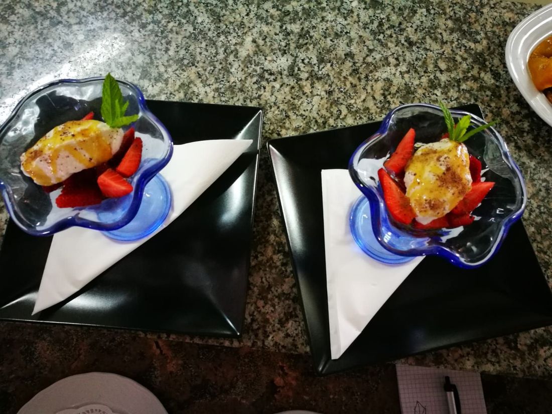 Due dessert in ciotole di vetro con bordo blu, con fragole e un rametto di menta su piatti neri, su una superficie di granito.