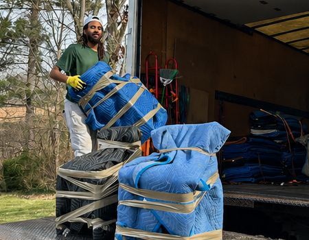 Stacks of packed cardboard boxes and wrapped furniture clutter a covered driveway, ready for moving.