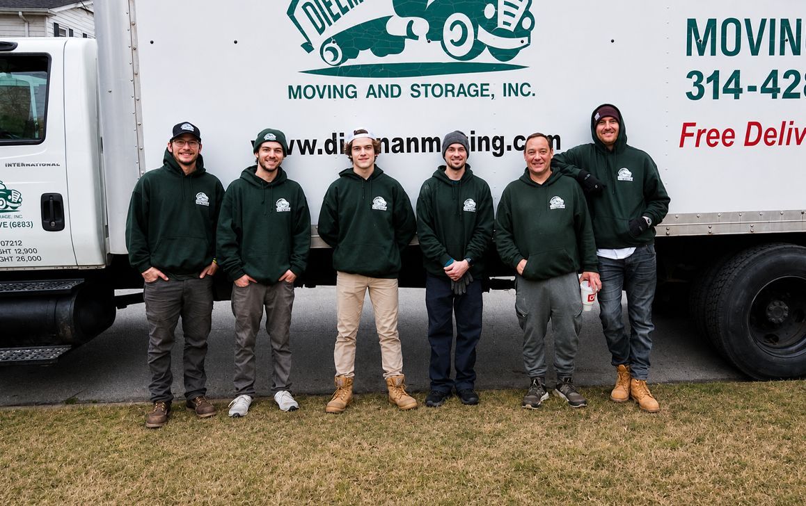 Six workers in dark green hoodies stand in front of a white moving truck.