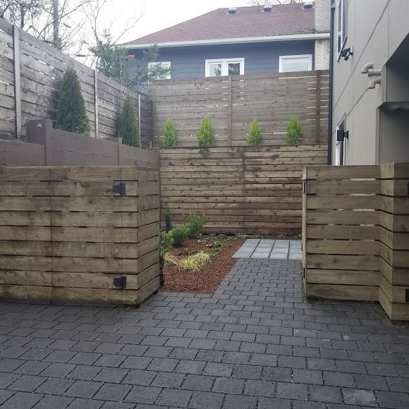 A brick driveway with a wooden fence and a house in the background.