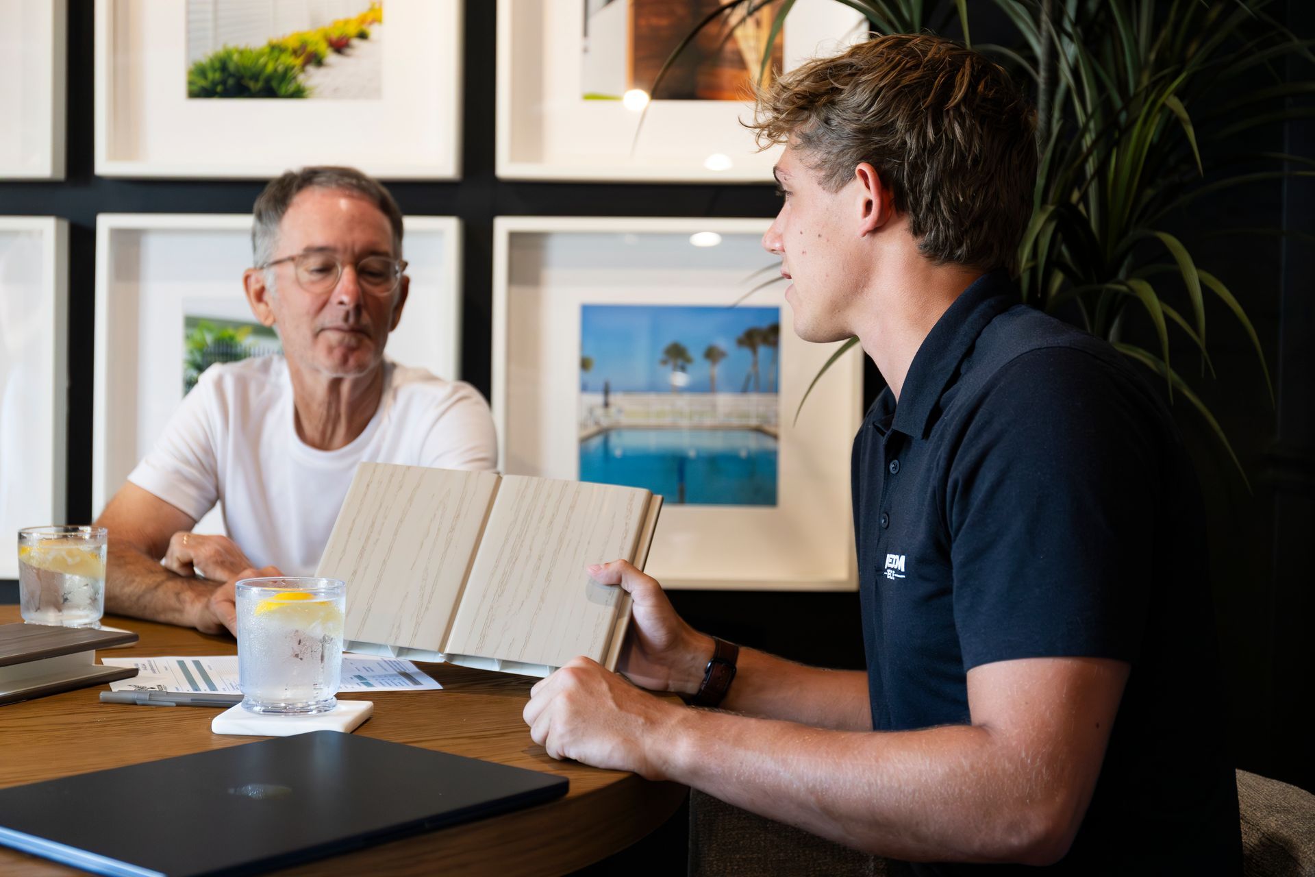 Two people sitting at a table in a bright room, one holding an open planner and gesturing to the other.