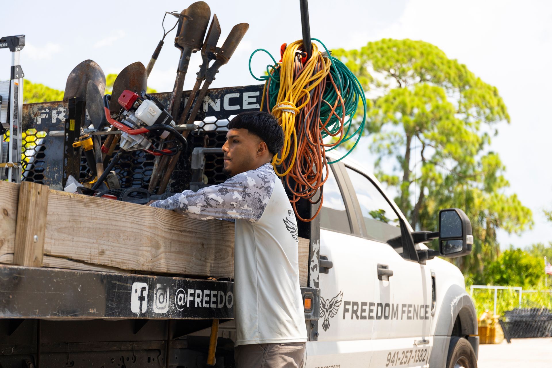 A worker in a patterned shirt stands next to a truck bed loaded with shovels, gear, and rope for Freedom Fence.