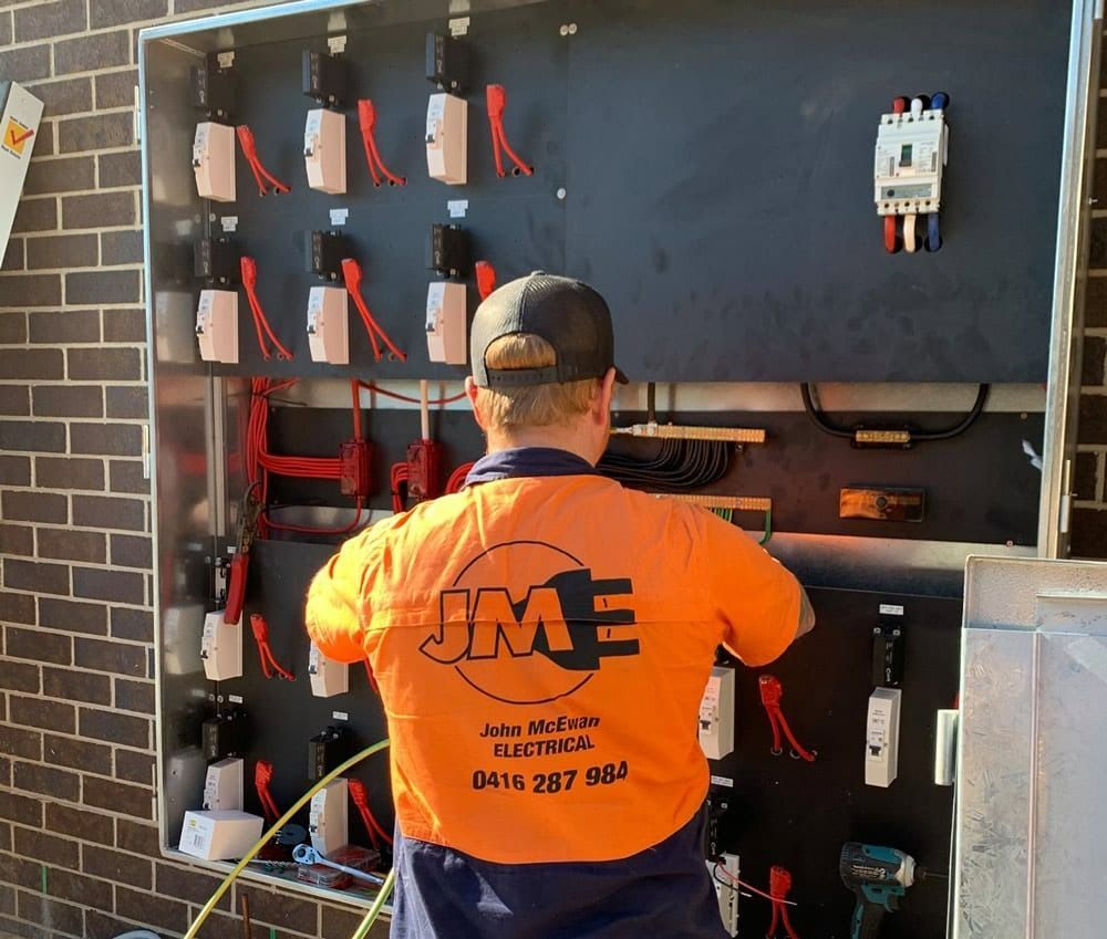 A Man Wearing a Orange Shirt is Working on an Electrical Box — John McEwan Electrical in Dapto, NSW