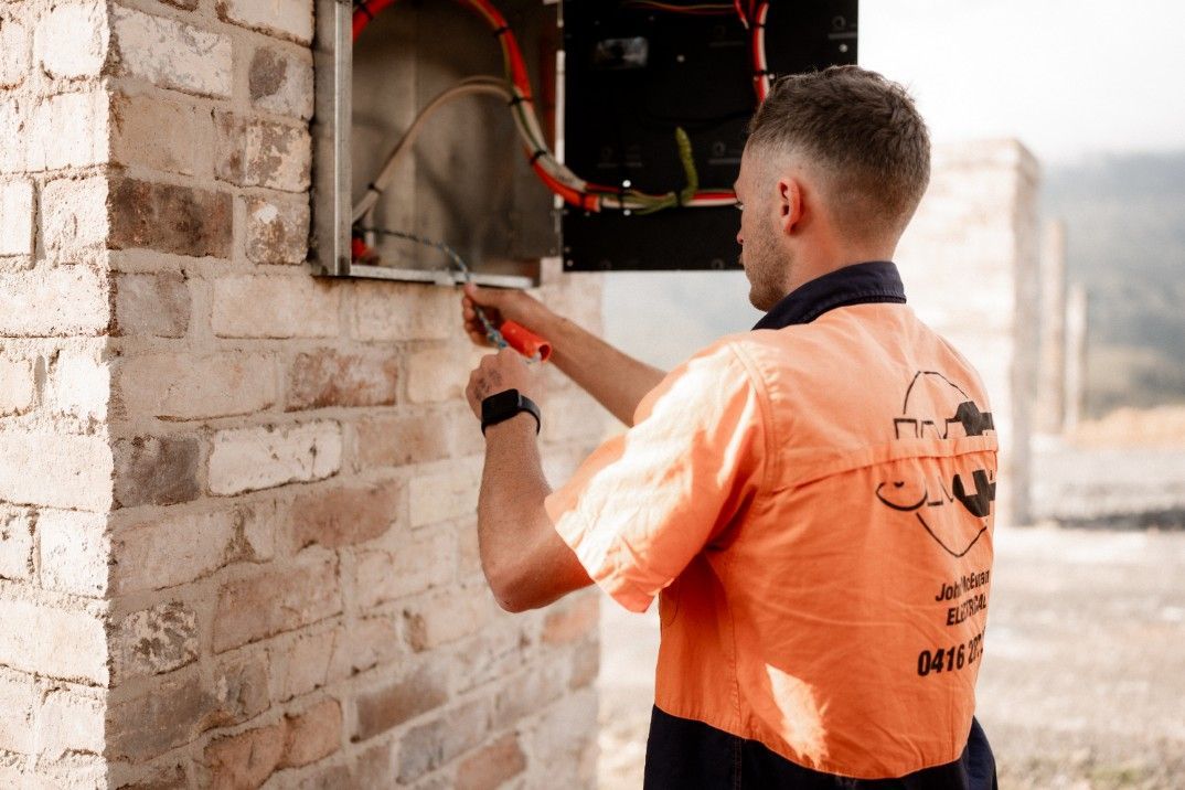 A Man is Working on an Electrical Box on a Brick Wall — John McEwan Electrical in Dapto, NSW