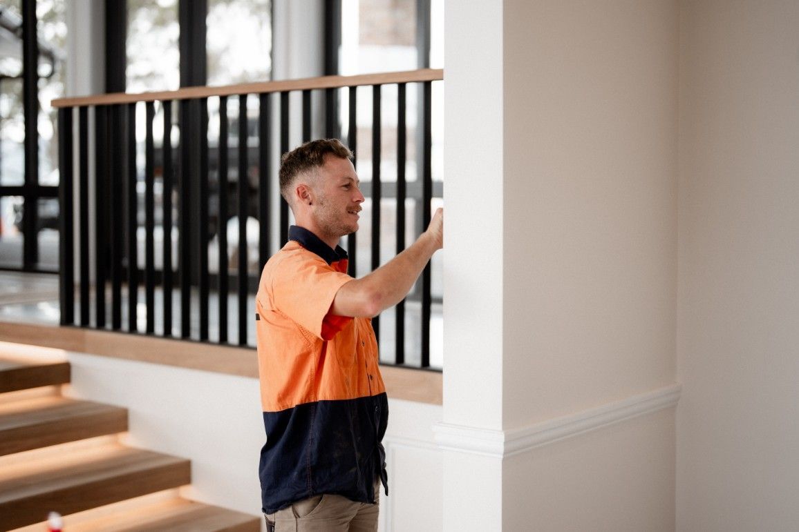 A Man in an Orange Shirt is Standing Next to a Railing in a Room — John McEwan Electrical In Dapto, NSW