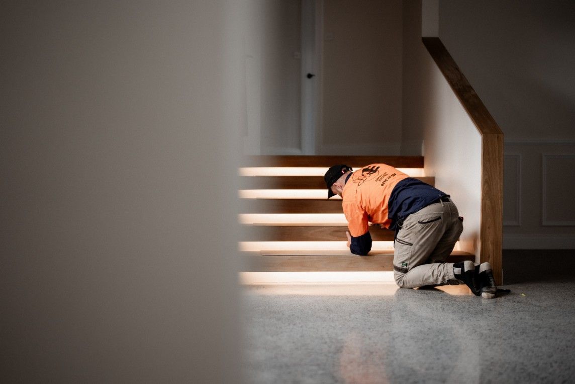 A Man is Kneeling Down on the Floor in Front of a Stairs — John McEwan Electrical in Shellharbour, NSW