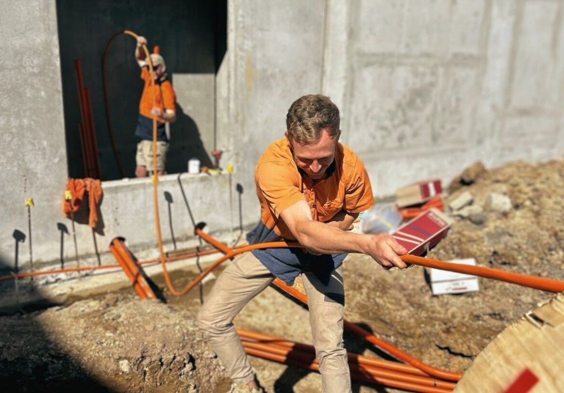 A Man in an Orange Shirt is Working in the Dirt — John McEwan Electrical in Dapto, NSW