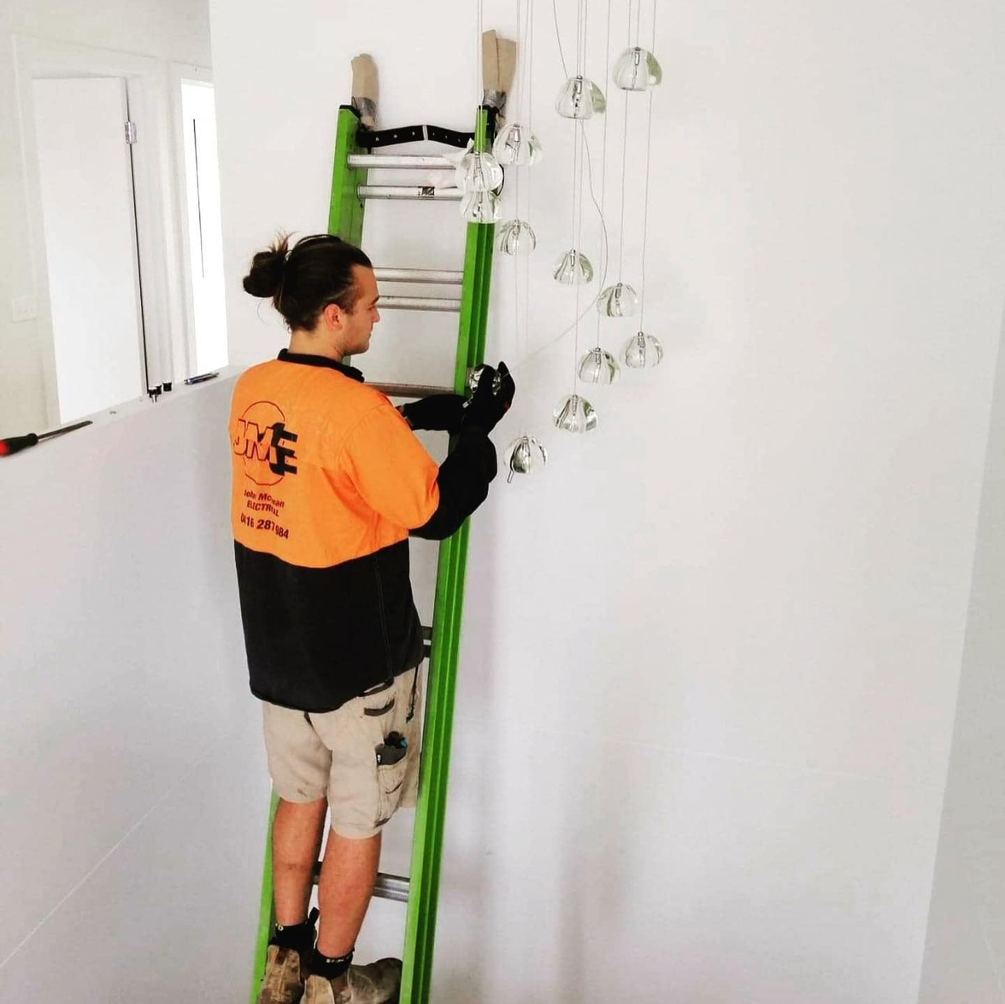 A Man Standing On A Green Ladder With A Shirt — John McEwan Electrical In Albion Park, NSW