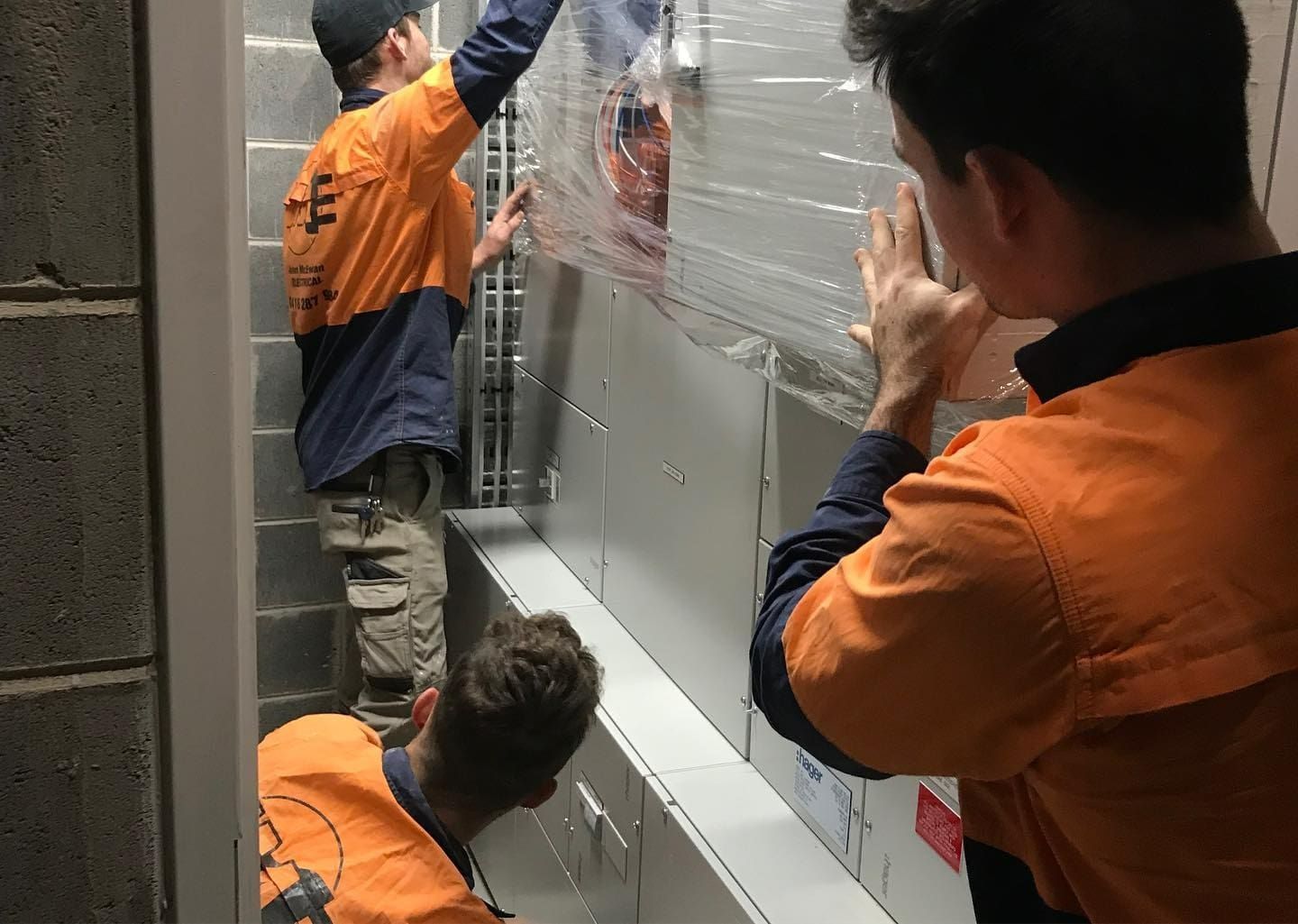 Two Men Are Wrapping A Wall With Plastic Wrap — John McEwan Electrical In Unanderra, NSW