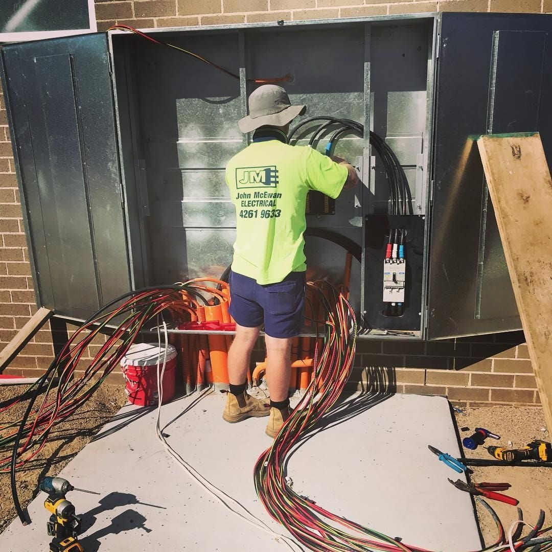 A Man In A Yellow Shirt Is Working On Electrical Wires — John McEwan Electrical In Shellharbour, NSW